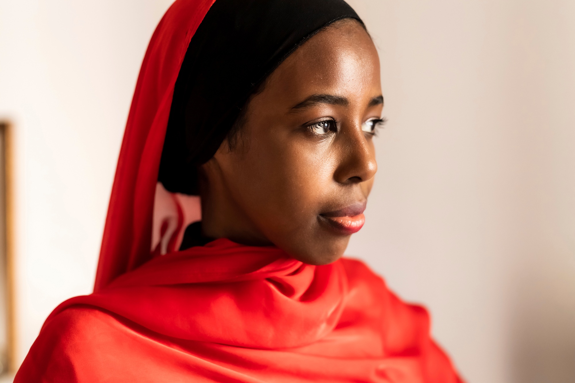 Young woman in contemplation wearing a vibrant red hijab.